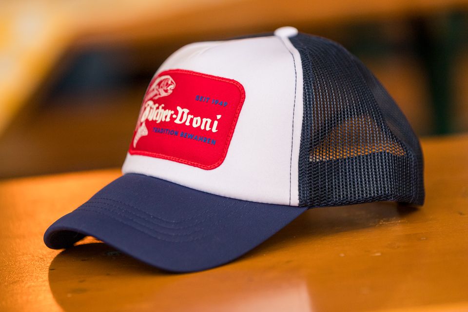 Trucker-Cap in Navy und Weiß mit rotem Fischer-Vroni-Patch auf einem Biertisch